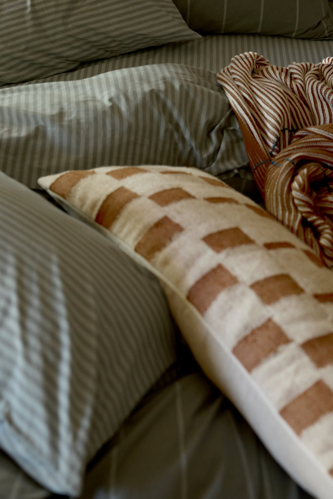 Bed with striped pillows and a checkered pillow on a neutral background