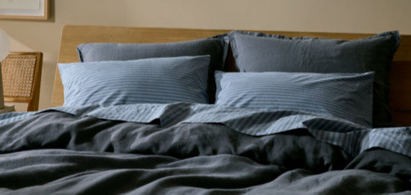 Bed with dark blue bedding and striped pillows in a room setting.